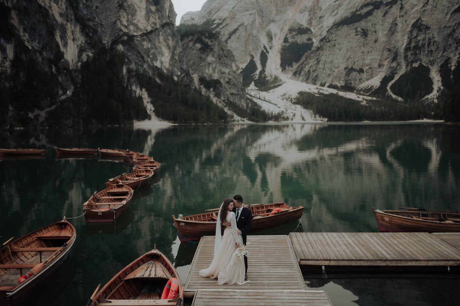 Bride and groom at Lake Braies in the Dolomites with boats on the lake during Italy Elopement